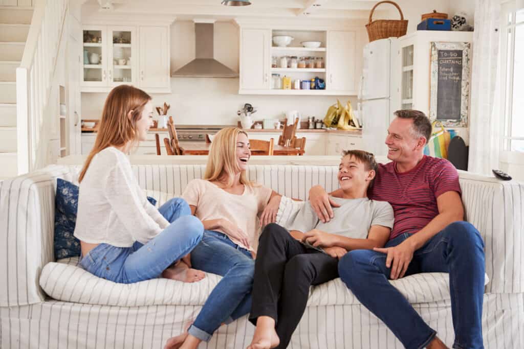 Two foster parents sitting on the couch laughing with their two foster children.