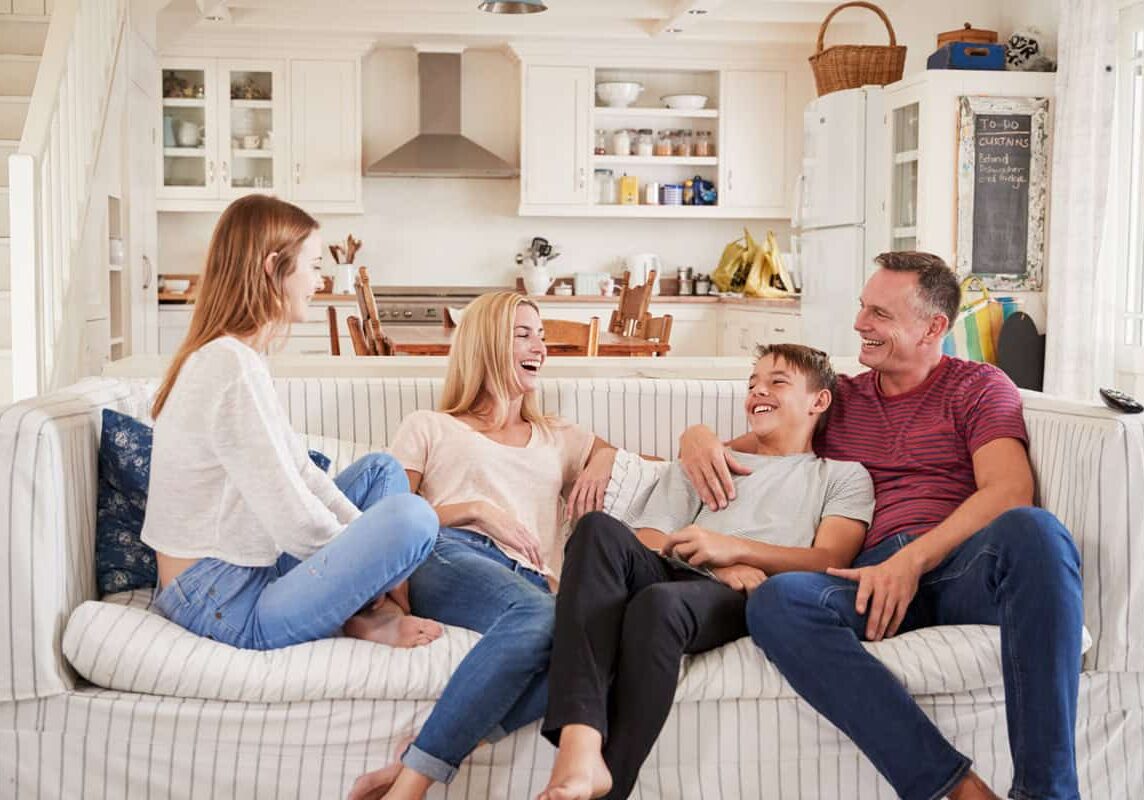 Two foster parents sitting on the couch laughing with their two foster children.